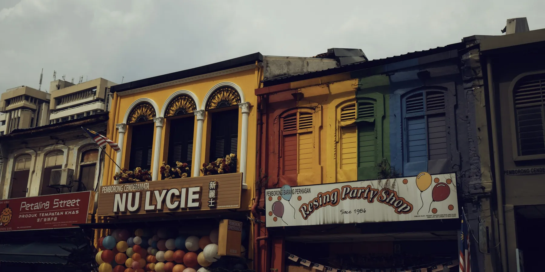 A row of restored yellow and blue shophouses on Petaling Street with painted shop signboards.