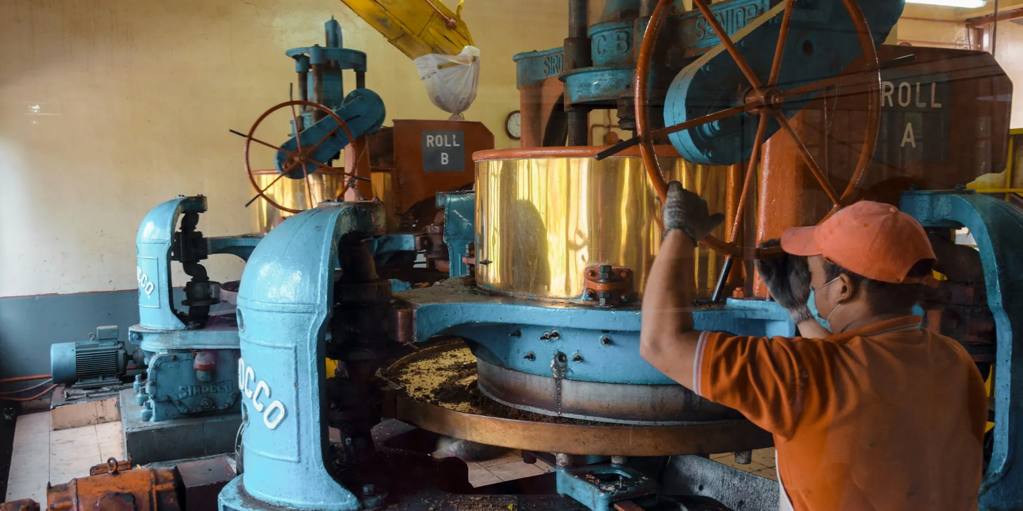 A machine operator working a large blue industrial press in a Malaysian workshop.