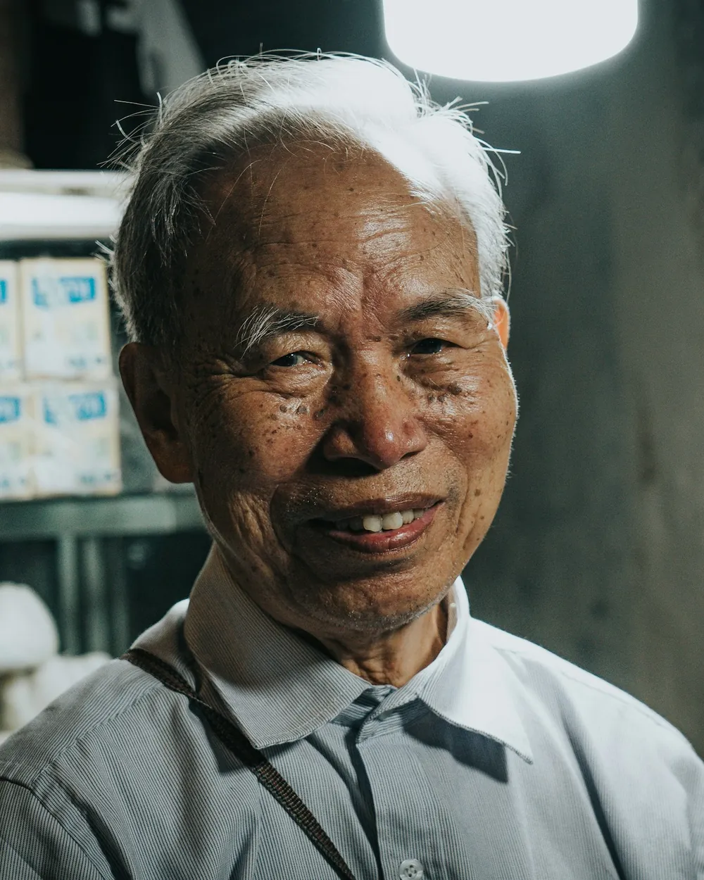 An older shopkeeper smiling, photographed against a dark interior.