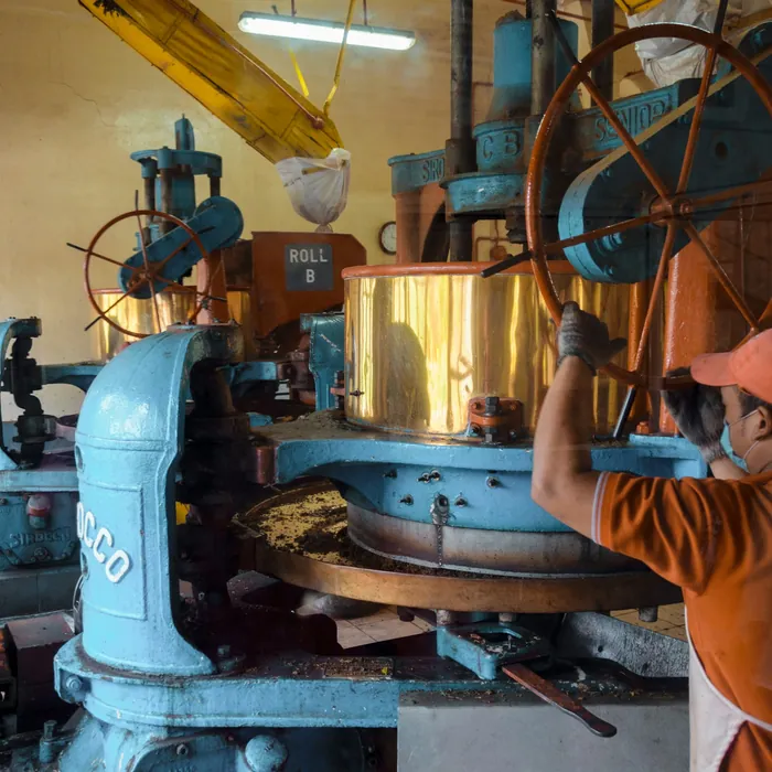 A machine operator working a large blue industrial press in a workshop.